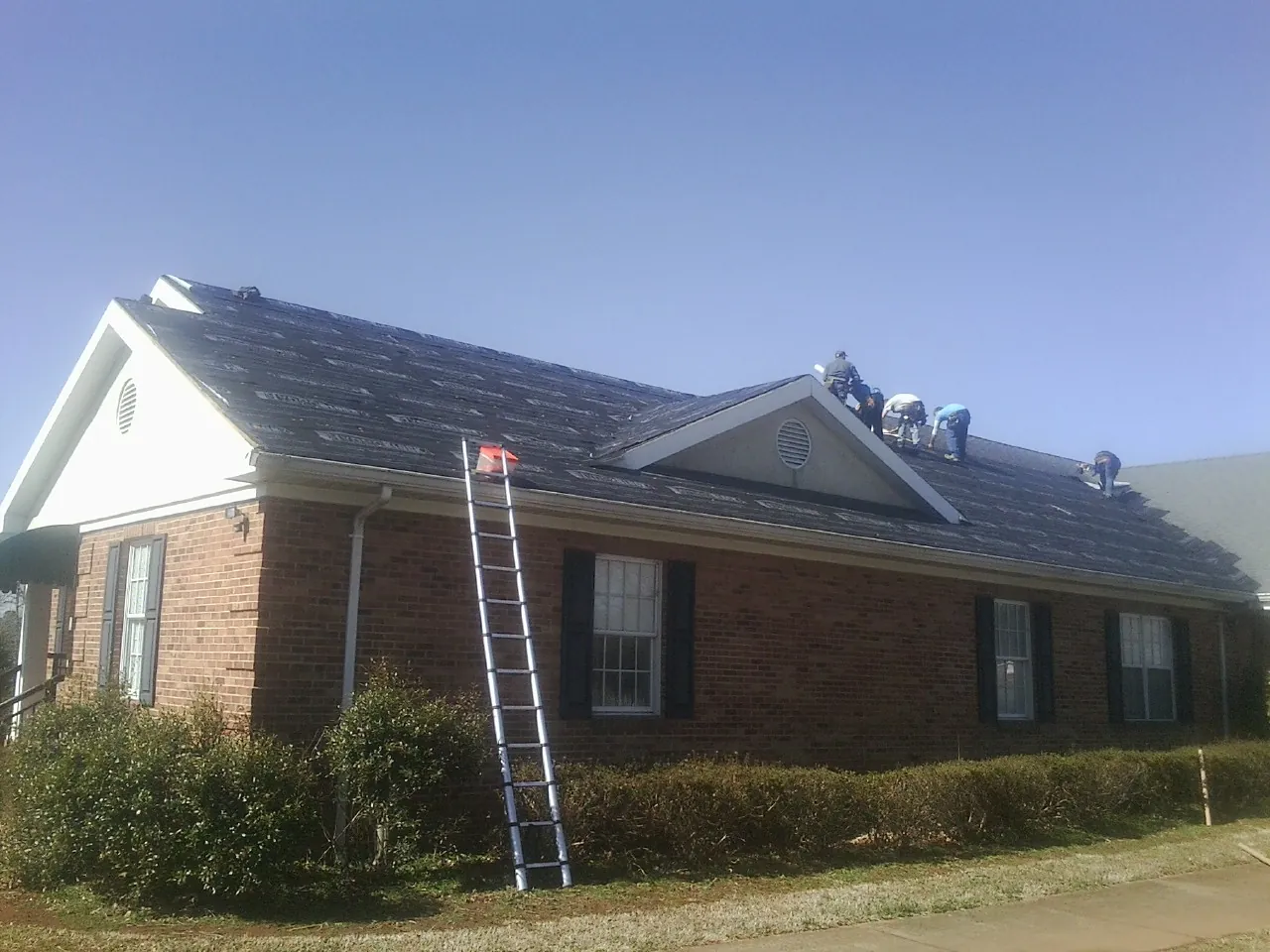 Crew tearing shingles off a brick ranch roof with a ladder set — Metal Roof Repair work by our crew in Fresno